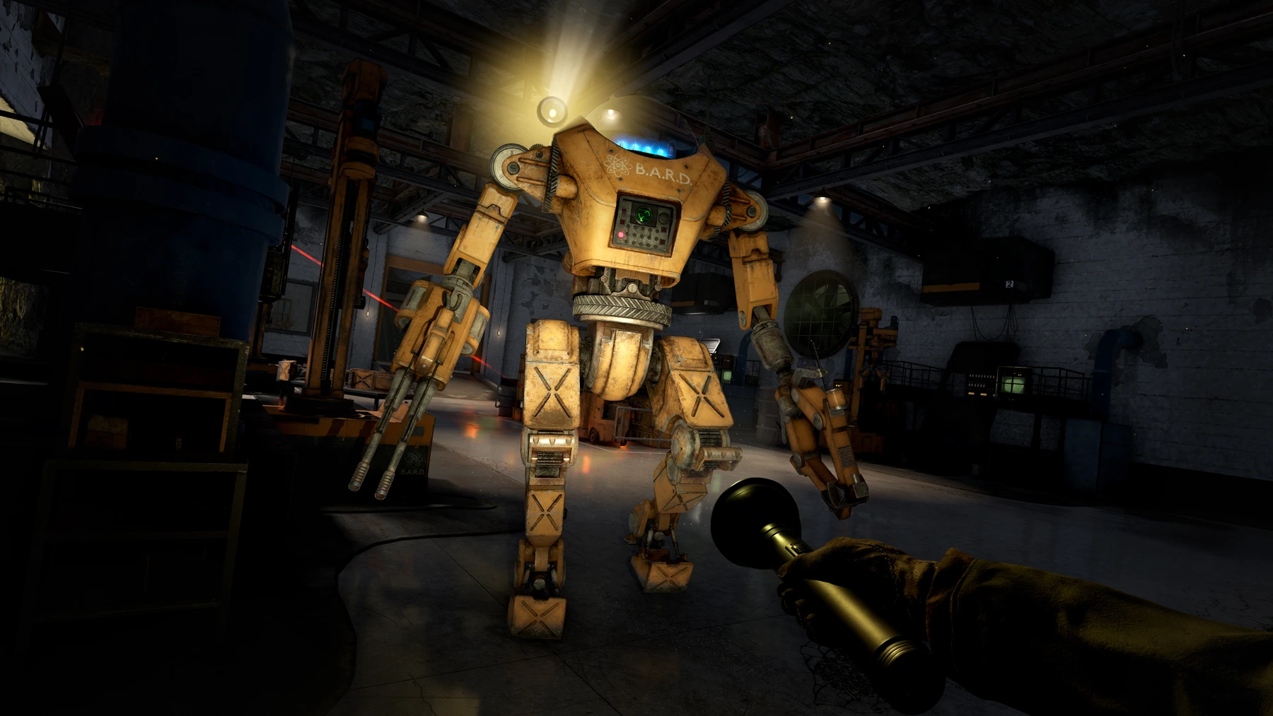 A screenshot with a torch being pointed at a large orange robot patrolling in an industrial basement. Across the robot’s chest is an icon of an atom and the text B.A.R.D. Around the room are storage crates, old-fashioned computer monitors, and other industrial pipes and tanks. In the background a red laser can be seen shining across the room.